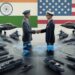 India and the United States shaking hands over a futuristic military command table, with fighter jets, helicopters, naval warships, artillery syst